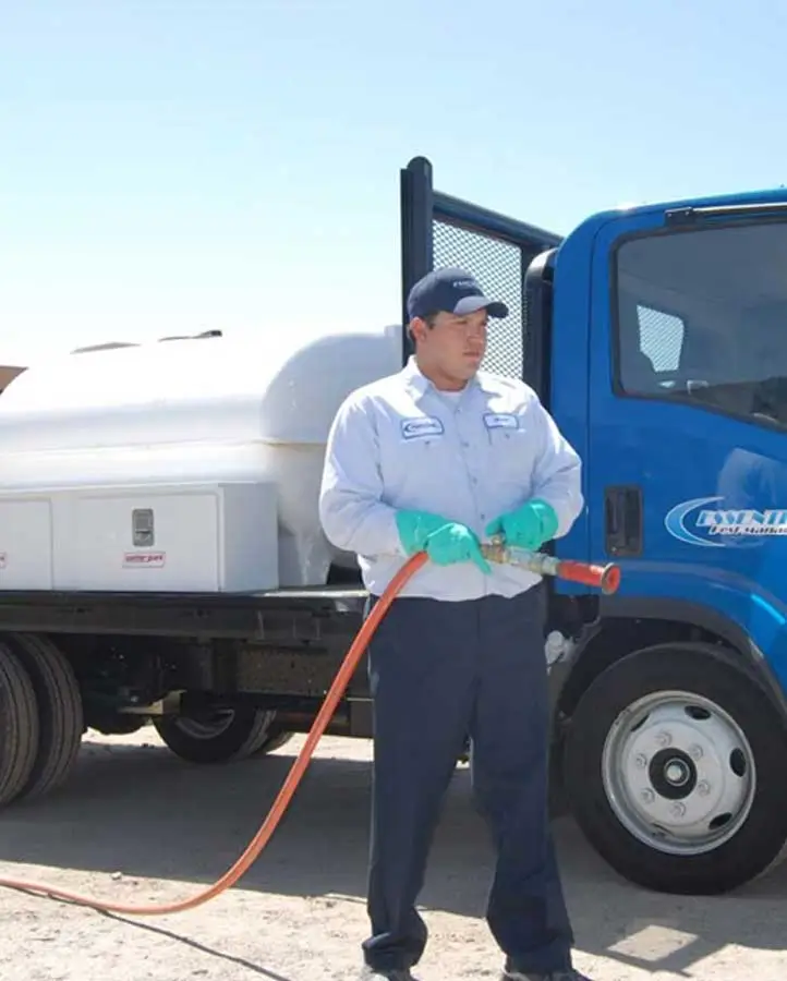A man in a blue uniform and hat standing next to a large blue truck, holding a fuel hose and refueling the vehicle.