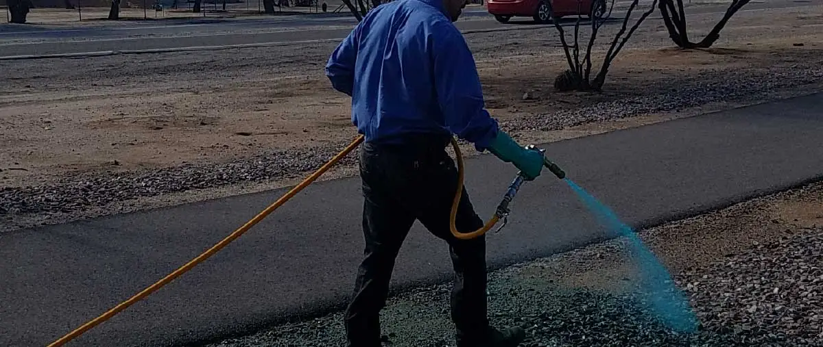 The image shows a worker using a hose to spray water on the ground in an outdoor setting, likely for cleaning or landscaping purposes.